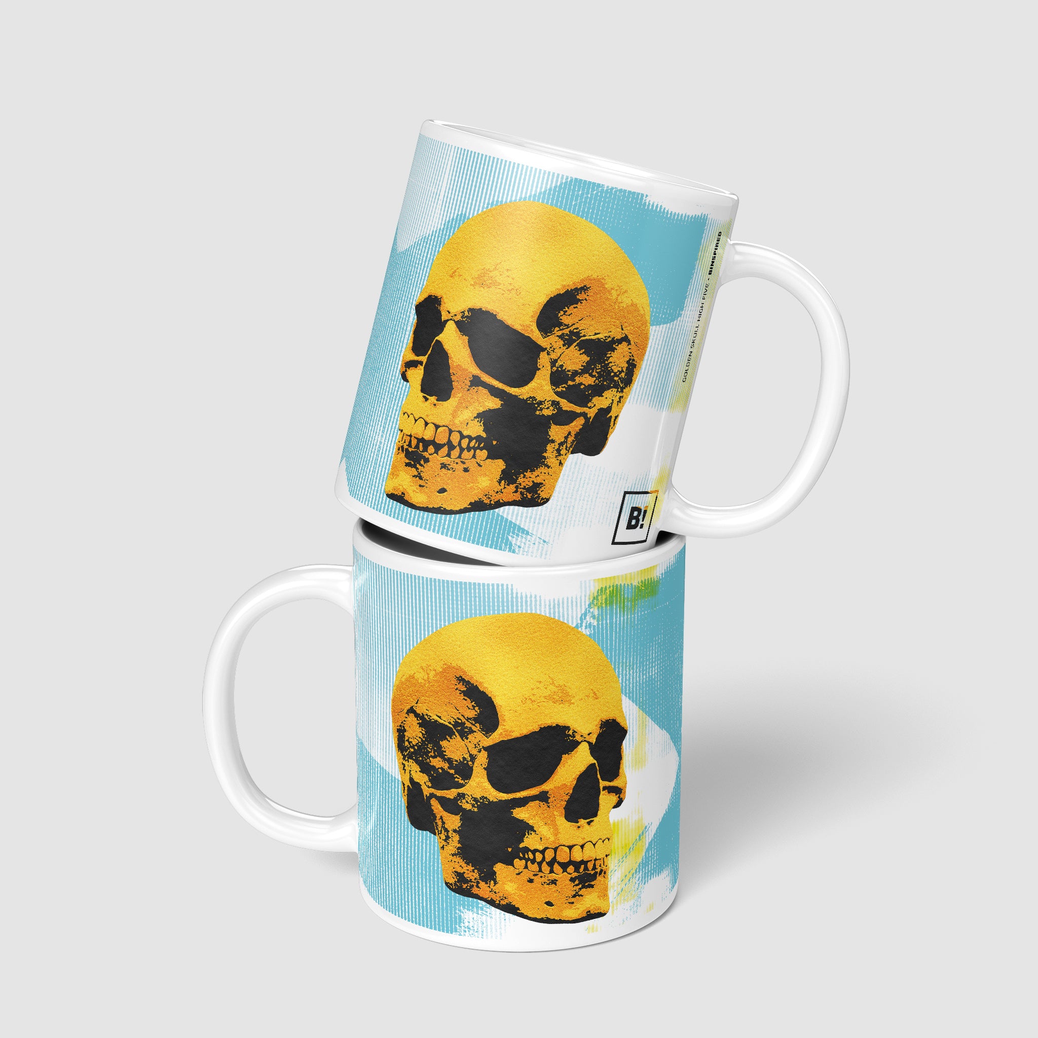 Two 11oz Golden Skulls High Five coffee mugs stacked, showing both sides of the vibrant pop art design with golden skulls high-fiving against a light blue abstract background.